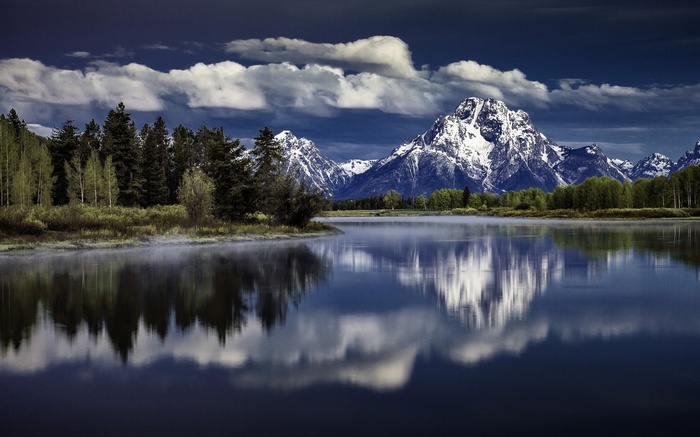 Snow-capped mountains reflected in a calm lake with trees