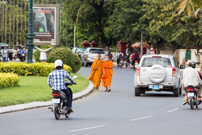 Monks walking on street with motorcycles and cars