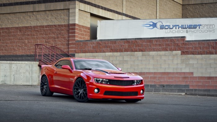 Red Chevrolet Camaro parked in front of a brick building
