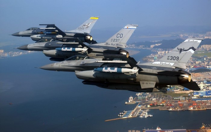 Four F-16 Fighting Falcons fly in formation over a city and harbor