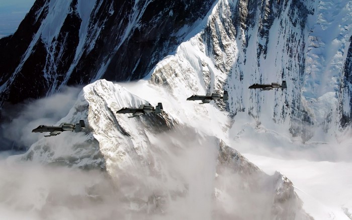 Four A-10 Thunderbolt II aircraft fly over snowy mountains