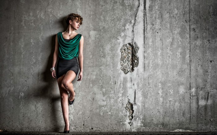 Woman in green top and black skirt leaning against concrete wall