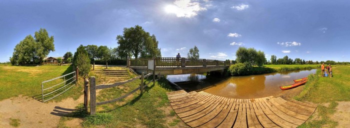 Bridge over a river with canoes and a building