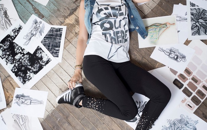 Woman in denim vest and leggings surrounded by fashion sketches
