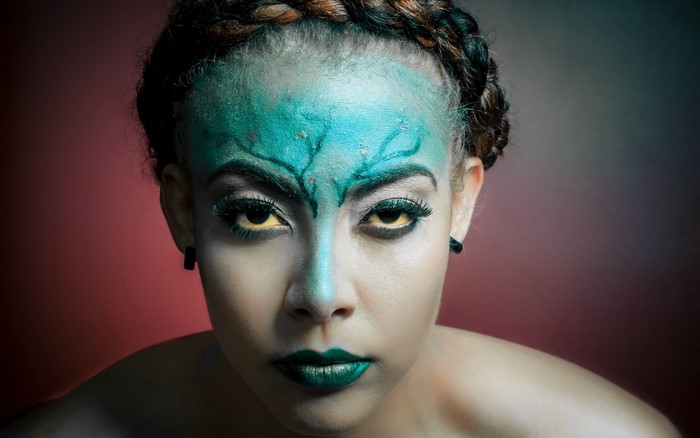 Woman with green and blue face paint and yellow eyes