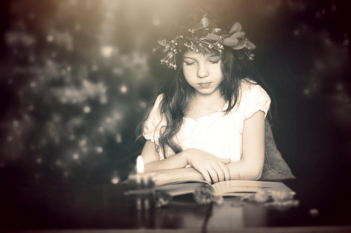 Girl with flower wreath reading a book by candlelight