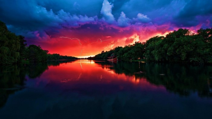 Lightning strikes over a lake at sunset with colorful clouds