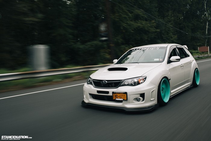 White Subaru Impreza WRX STi with teal wheels on a road
