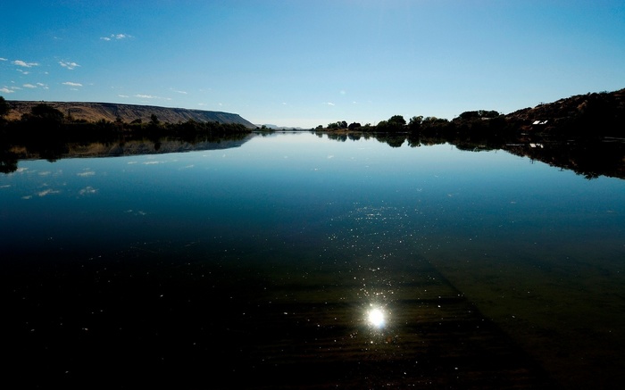 Calm lake reflecting a clear blue sky and distant hills