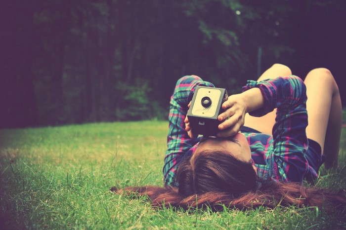 Woman lying on grass taking a photo with a camera