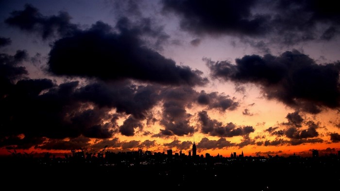 Dark clouds over a city skyline at sunset