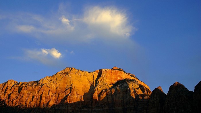 Mountain range illuminated by sunset under a blue sky with clouds