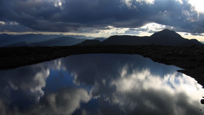 Mountain lake reflecting dramatic clouds and peaks