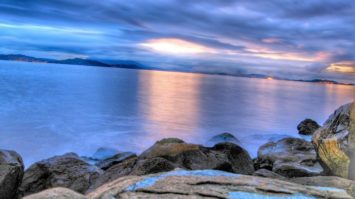 Rocky shore with calm water and cloudy sky at dusk