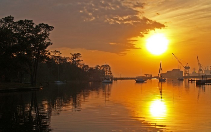 Sunset over a harbor with boats and cranes