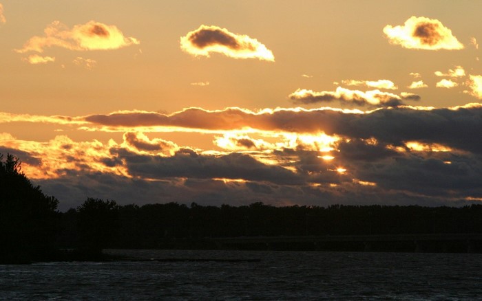 Sunset over water with clouds and trees