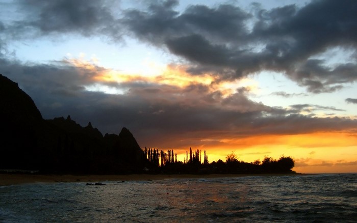 Sunset over a tropical beach with mountains and ocean waves