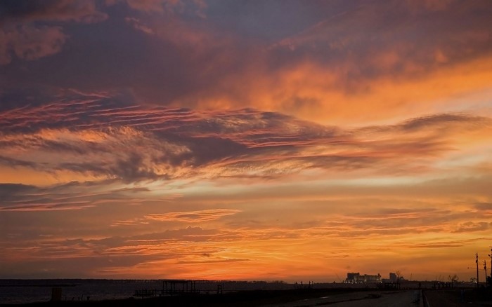 Sunset over the sea with colorful clouds and distant city