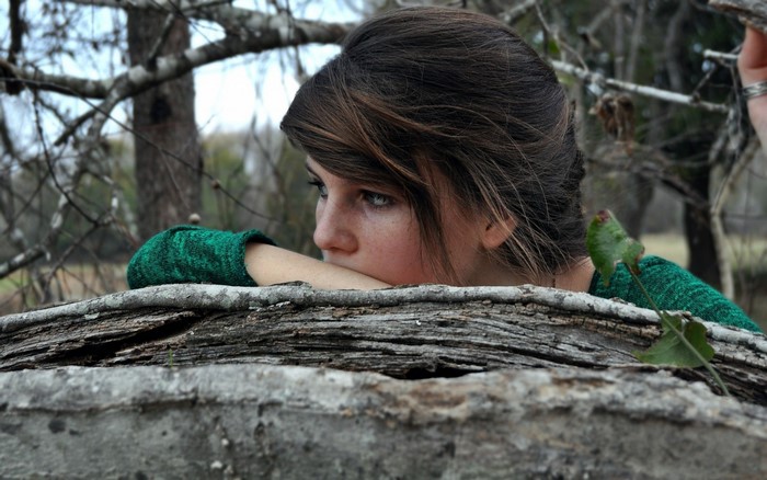 Young woman with brown hair wearing green sweater in forest
