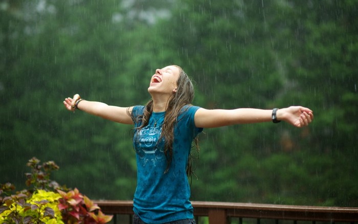 Young woman enjoying the rain with arms outstretched