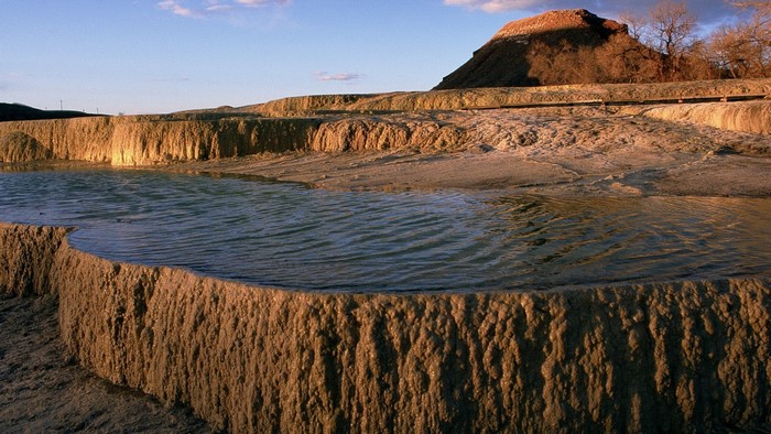 Terraced mineral formations with water and a hill at sunset
