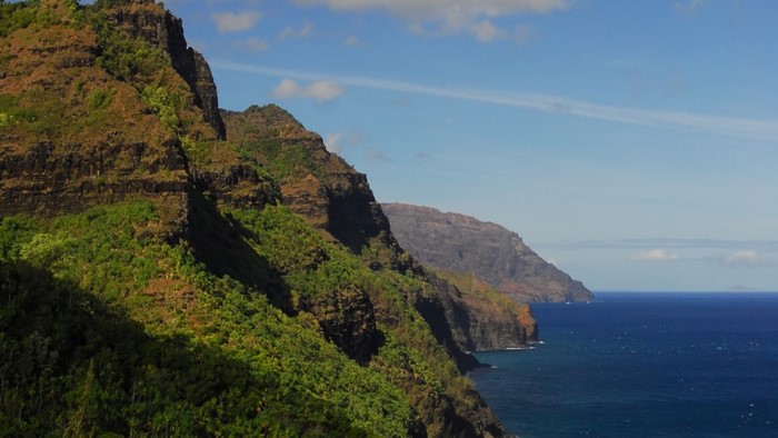 Rugged green mountains meet the blue ocean under a cloudy sky