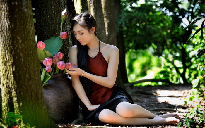 Woman in Red Dress Sitting by Tree with Lotus Flowers