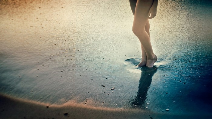Woman's legs standing in shallow sea water on a beach