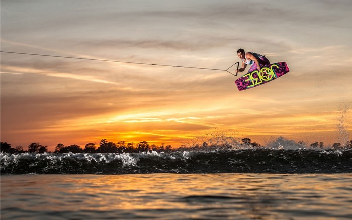 Man wakeboarding during sunset over waves