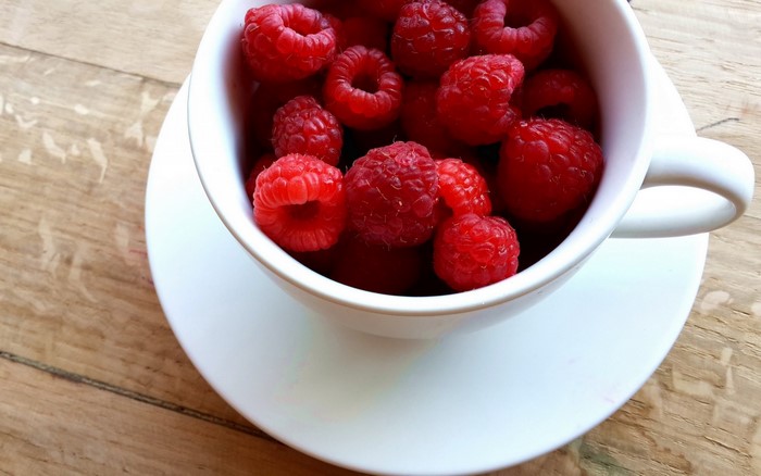 Raspberries in a white cup on a saucer