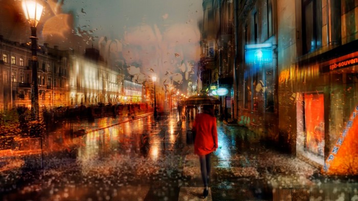 Woman in red coat walks on rainy city street at night