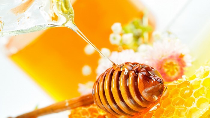Honey dripping from a dipper onto honeycomb and flowers