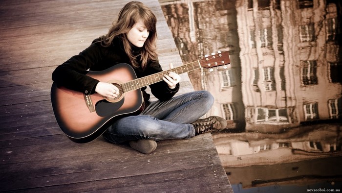 Woman playing guitar on a wooden dock with building reflection