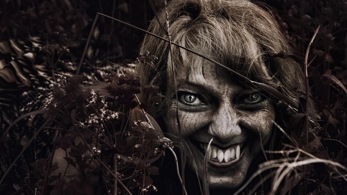 A frightening vampire with fangs emerges from foliage
