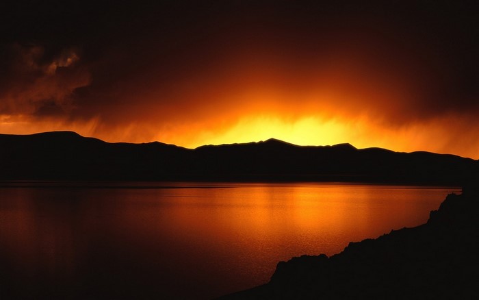 Sunset over a silhouetted mountain range and lake