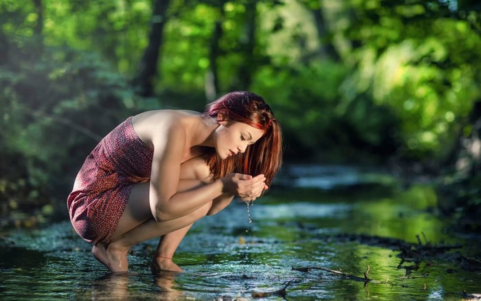 Woman drinking water from hands in forest stream