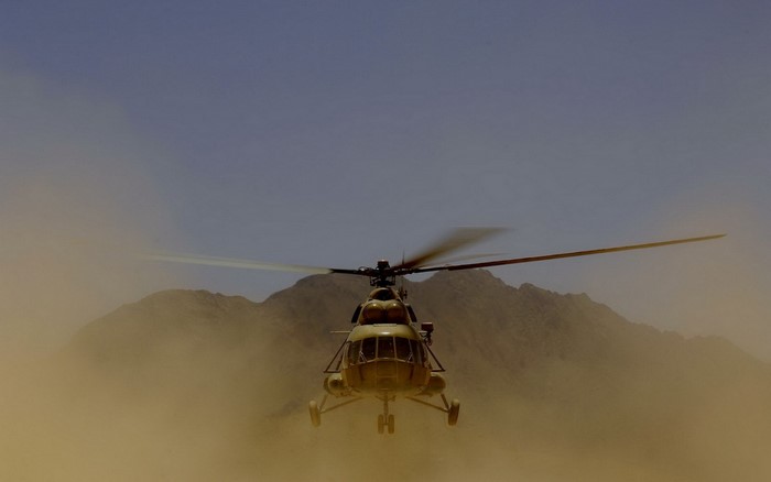 Military helicopter flying through dust near mountains