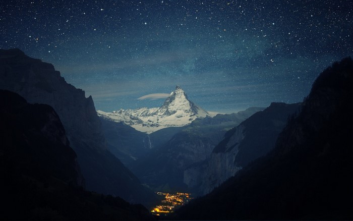 Matterhorn mountain at night with stars and a town in the valley