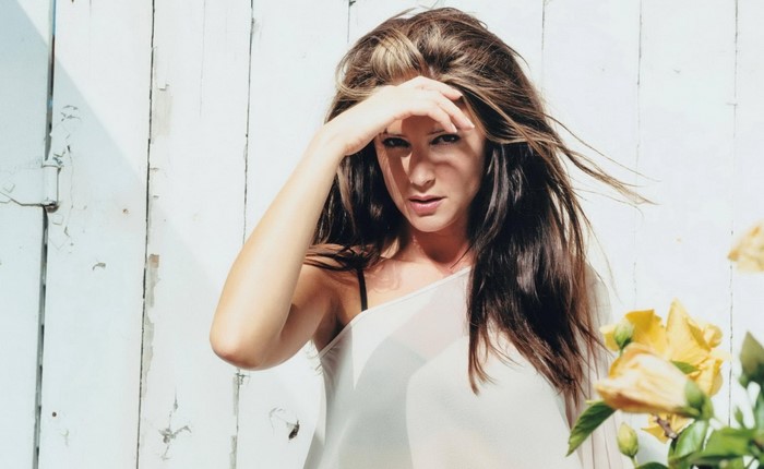 Woman with long brown hair in front of white wooden wall
