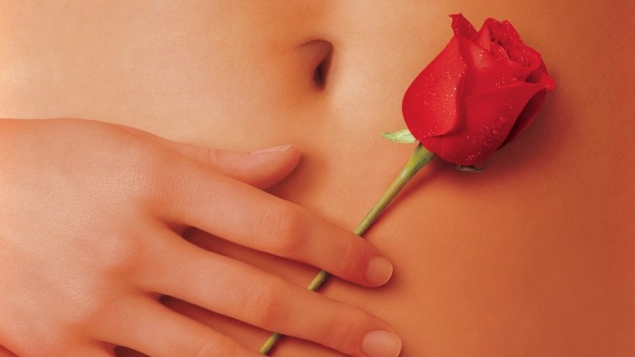 Close up of a hand and a red rose on a person's abdomen