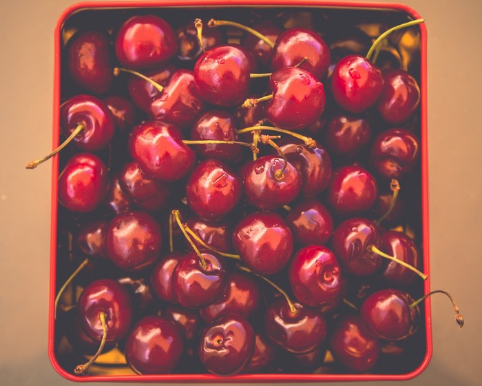 A close-up overhead view of fresh cherries in a red tin.