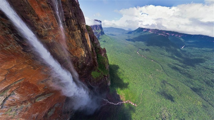 Waterfall cascading down a massive cliff into a lush green valley