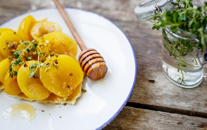 Sliced yellow fruit with honey and pistachios on a plate