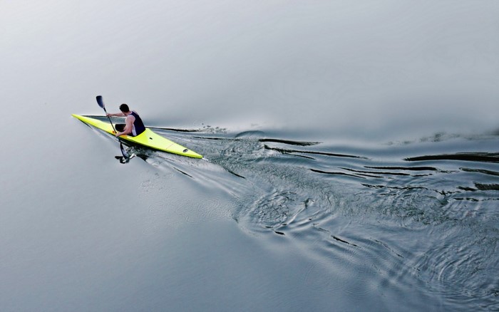 Man kayaking on calm water creating ripples