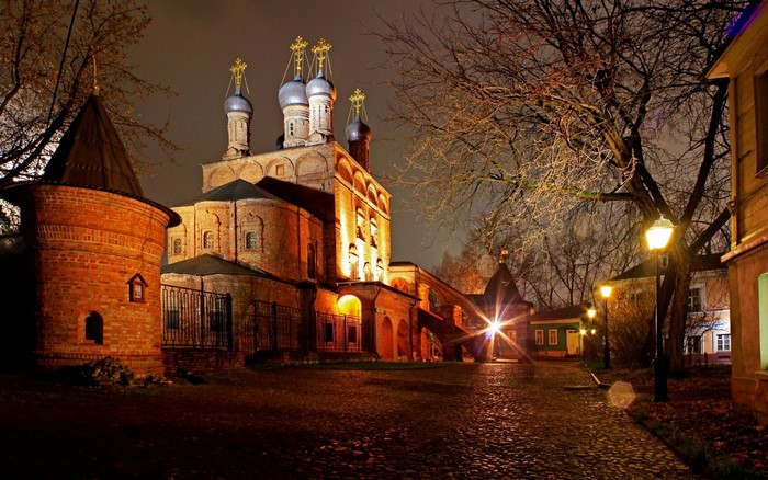 Night view of a historic brick church with onion domes and a cobblestone path.