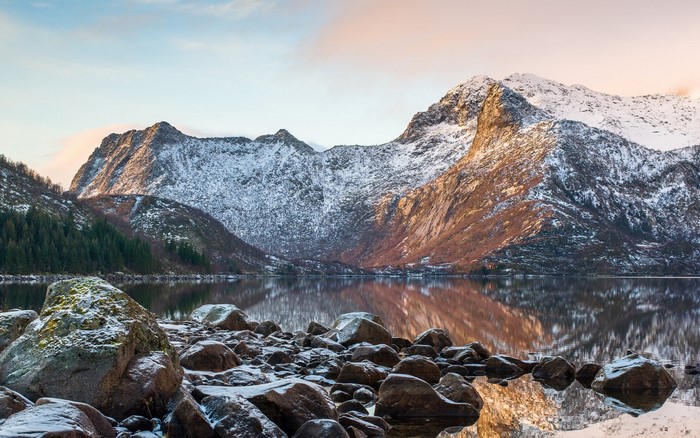 Snow-capped mountains reflected in a calm lake with rocks in the foreground