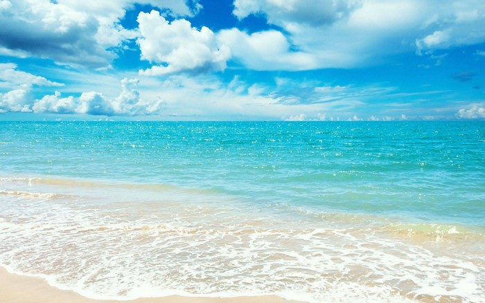 Turquoise ocean waves on a sandy beach under a cloudy blue sky