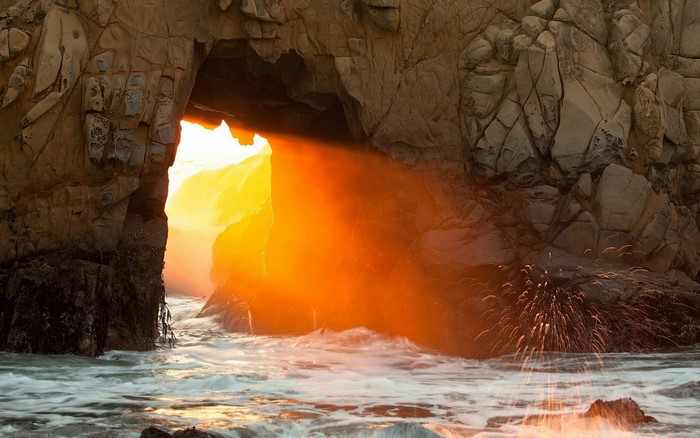 Sunlight streams through a sea cave archway onto the ocean.