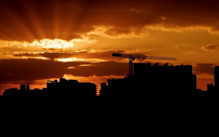 Sunset over a silhouetted cityscape with a construction crane