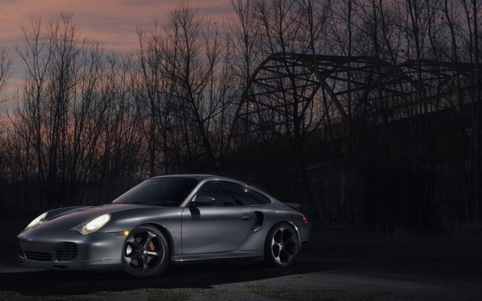 Silver Porsche 911 Turbo parked near a bridge at dusk